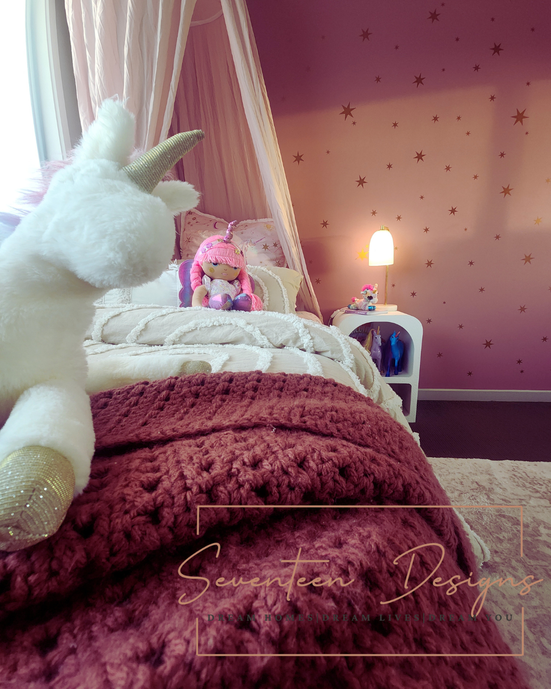 Cozy girls’ bedroom with a unicorn plush toy, pink canopy bed, star wall decals, and soft lighting. Kids' bedroom by Seventeen Designs.