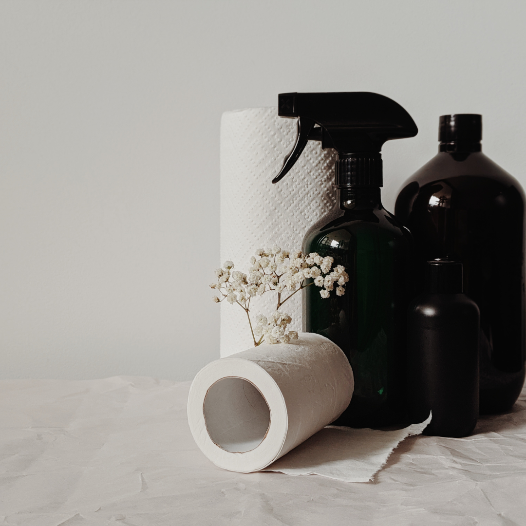 Minimalist cleaning supplies with glass spray bottles, paper towels, and a small white flower arrangement by Seventeen Designs